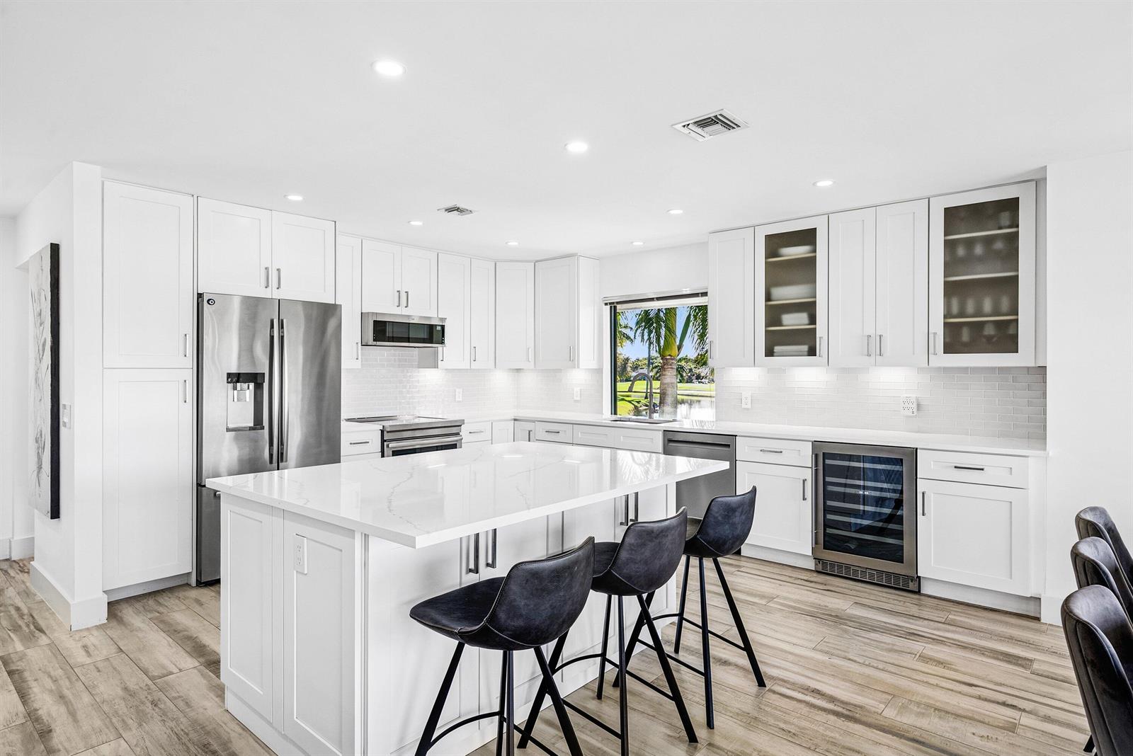 A modern white kitchen features a central island with bar stools and stainless steel appliances — 3667 Quail Ridge Drive N # B, Boynton Beach FL 33436, BOYNTON BEACH, FL