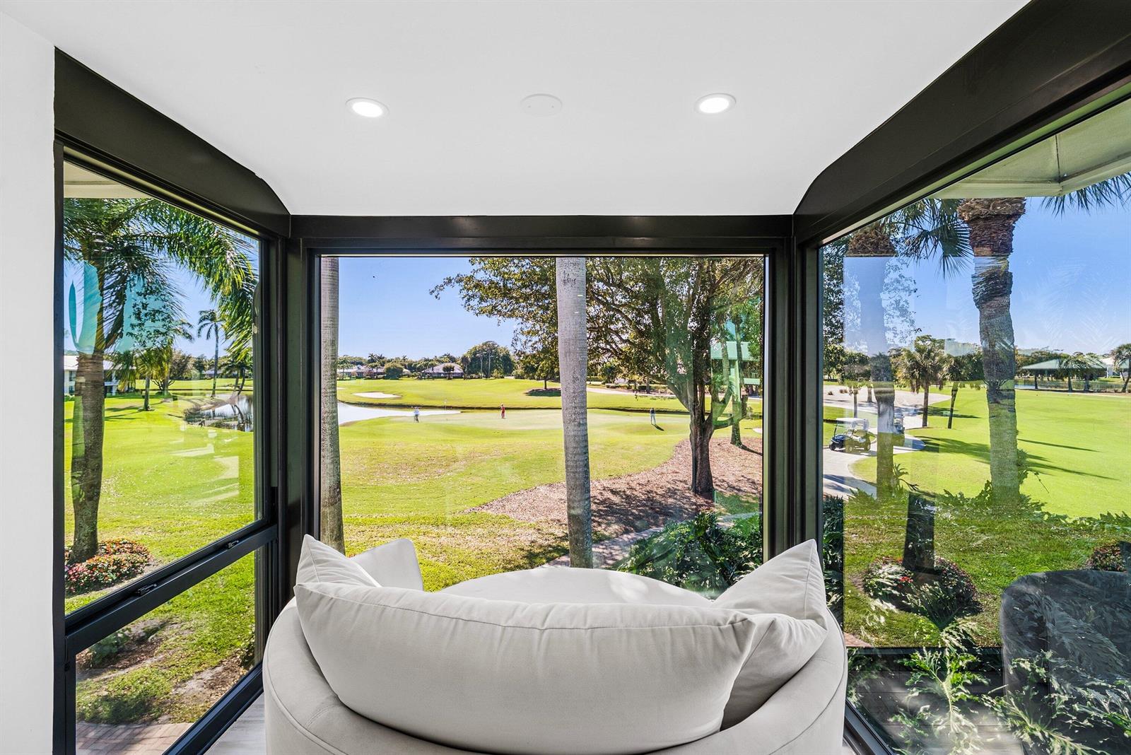 A sunroom with a circular chair overlooks a golf course through large glass windows — 3667 Quail Ridge Drive N # B, Boynton Beach FL 33436, BOYNTON BEACH, FL