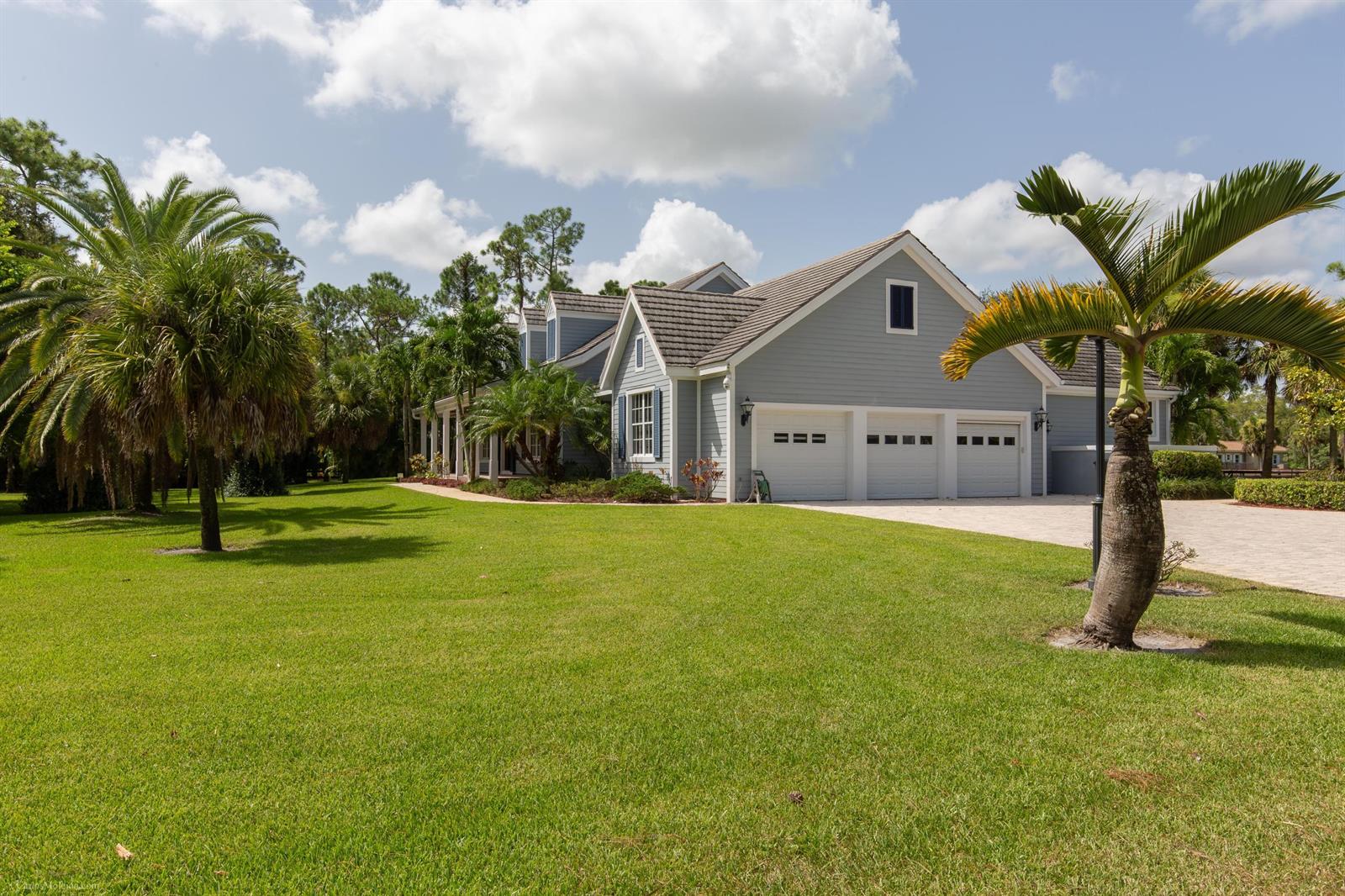 A light blue house with a three-car garage sits on a large, grassy lawn — 1321 Pelham Road, Wellington FL 33414, WELLINGTON, FL