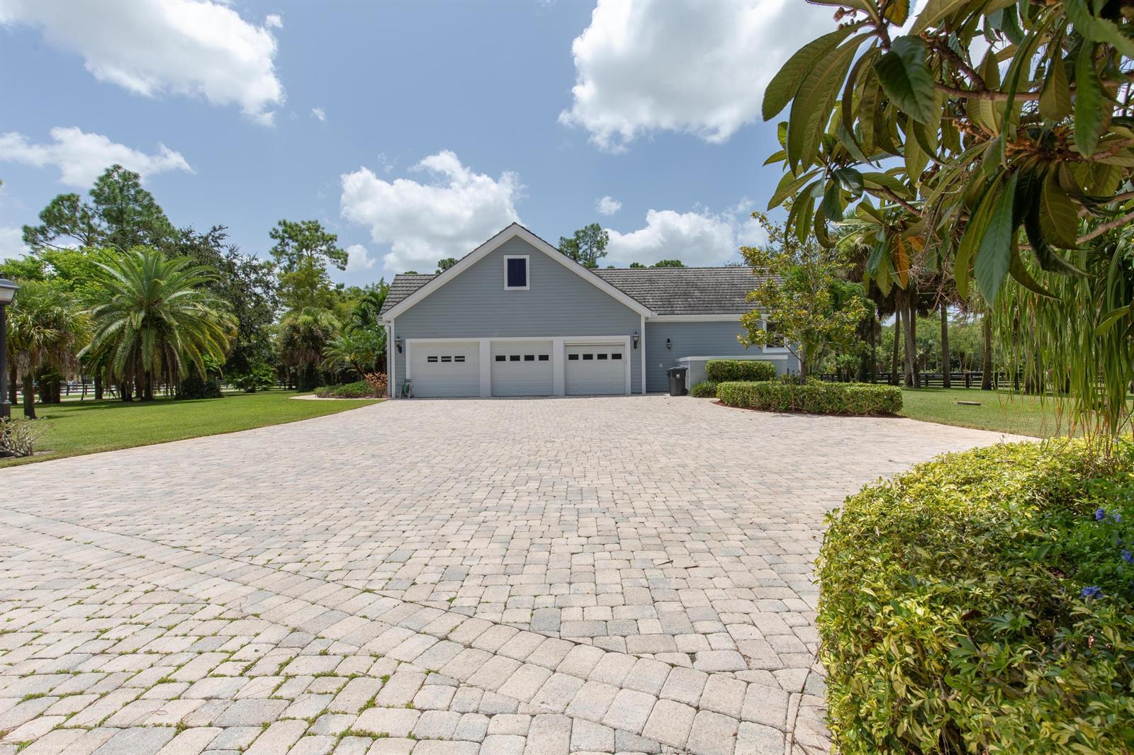 A light blue house with a three-car garage and a large paver driveway — 1321 Pelham Road, Wellington FL 33414, WELLINGTON, FL