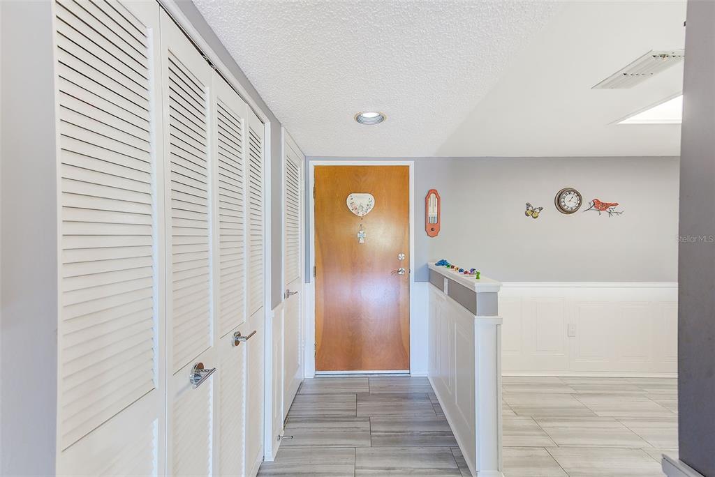 A foyer features a wood front door, louvered closet doors, and gray wood-look tile flooring — 2593 COUNTRYSIDE BOULEVARD UNIT 7206, CLEARWATER, FL