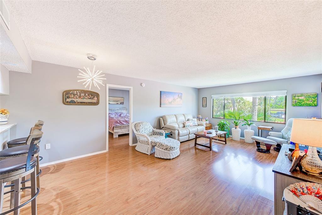 A living room with wood-look flooring, a white sofa, and a view of outdoor greenery — 2593 COUNTRYSIDE BOULEVARD UNIT 7206, CLEARWATER, FL