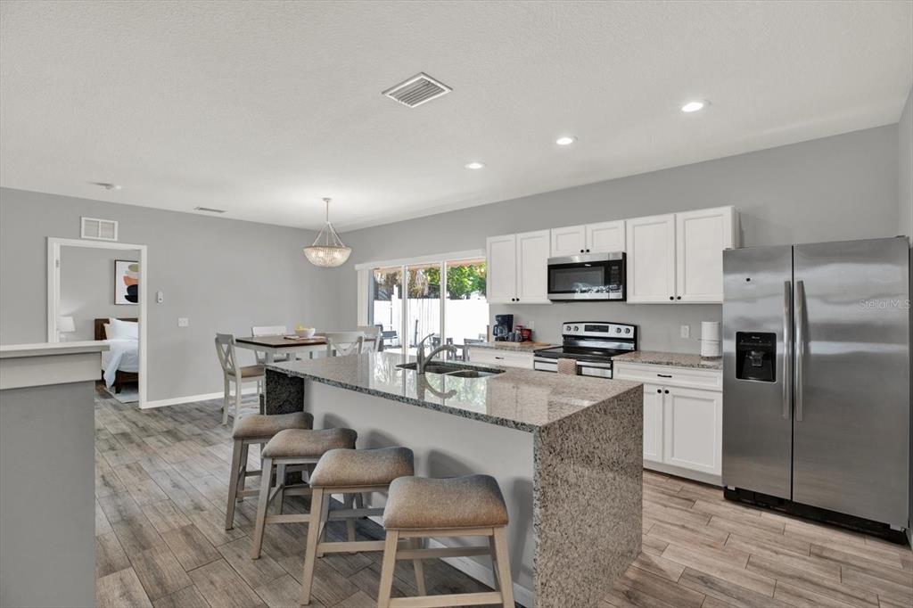 A kitchen features a granite-topped island, white cabinetry, stainless steel appliances, and wood-look tile flooring — 2011 OUTER DRIVE, SARASOTA, FL