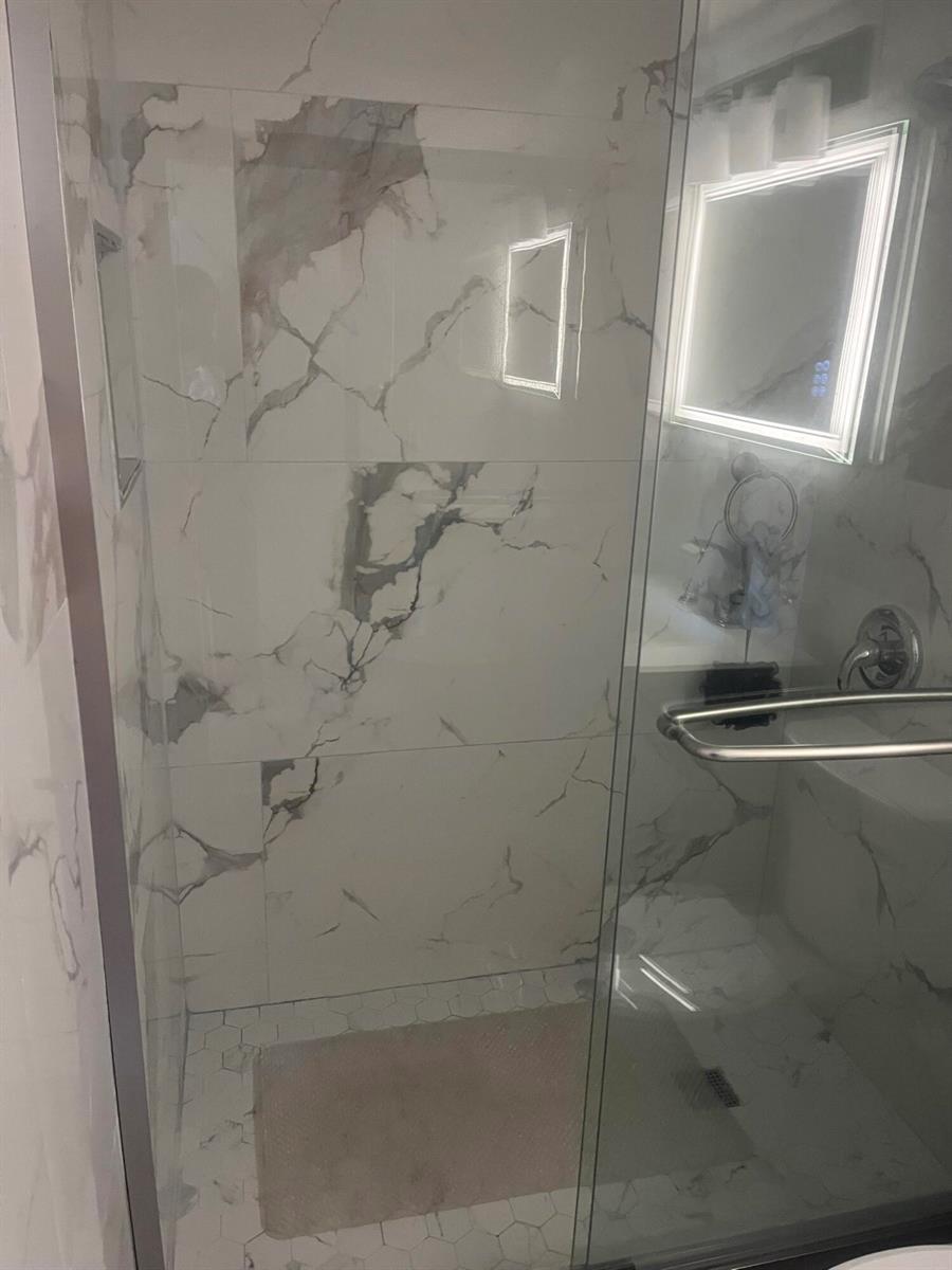 A glass-enclosed shower features white marble-look wall tiles and a hexagonal tile floor — 3531 Inverrary Drive # 308, Lauderhill FL 33319, LAUDERHILL, FL