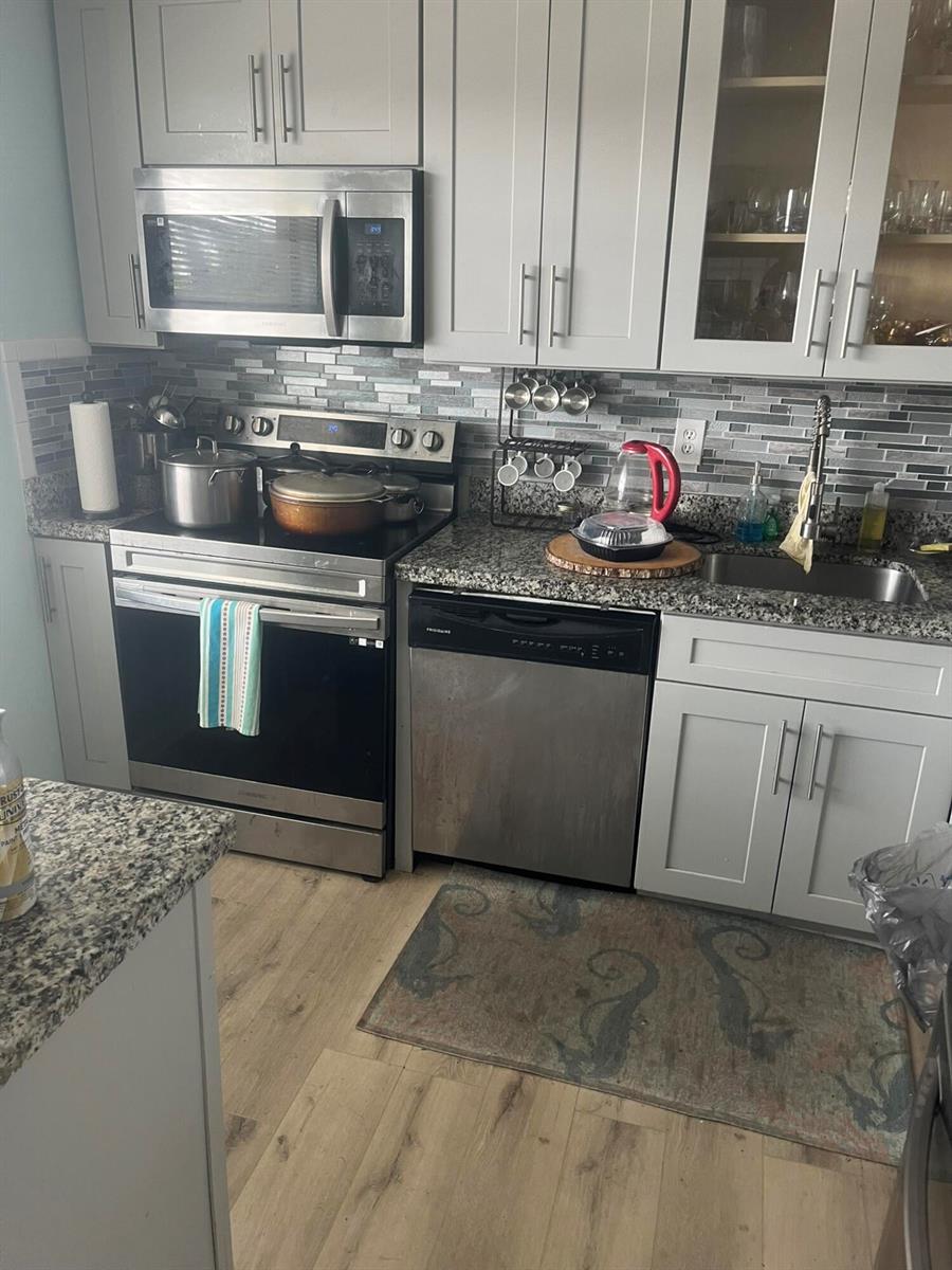 A kitchen features light gray cabinets, stainless steel appliances, granite countertops, and a tiled backsplash — 3531 Inverrary Drive # 308, Lauderhill FL 33319, LAUDERHILL, FL