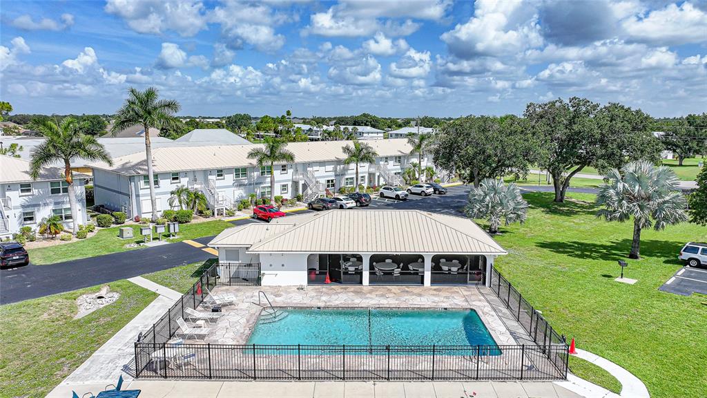 An aerial view shows a swimming pool with a patio and a clubhouse building nearby — 26485 RAMPART BOULEVARD UNIT D4, PUNTA GORDA, FL