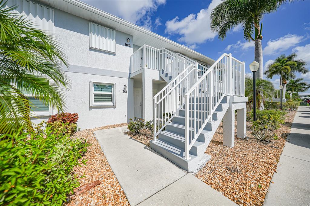 An exterior view of a two-story apartment building with white stairs and gravel landscaping — 26485 RAMPART BOULEVARD UNIT D4, PUNTA GORDA, FL