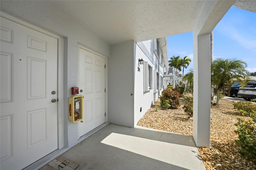 An exterior view of a covered apartment entryway with white doors and a fire extinguisher — 26485 RAMPART BOULEVARD UNIT D4, PUNTA GORDA, FL