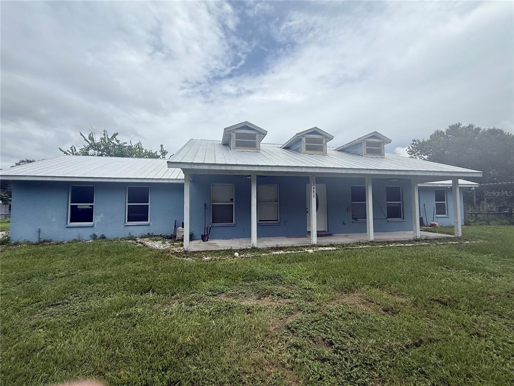A single-story blue house with a metal roof and three dormers features a front porch — 2480 NW GENES LITTLE ACRES AVENUE, ARCADIA, FL