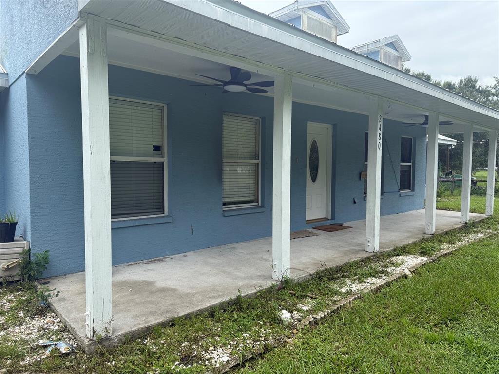 A blue house features a long covered front porch with white support columns — 2480 NW GENES LITTLE ACRES AVENUE, ARCADIA, FL