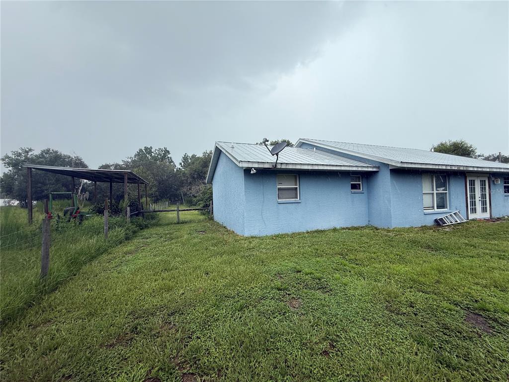 A blue house with a metal roof stands next to a covered outdoor structure — 2480 NW GENES LITTLE ACRES AVENUE, ARCADIA, FL