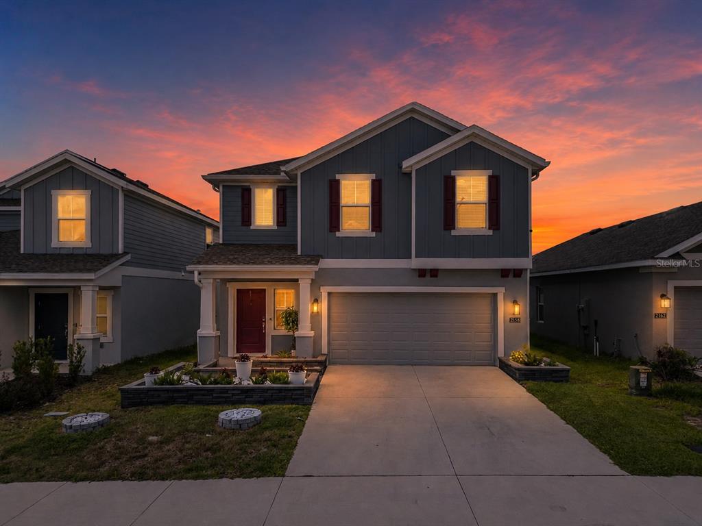 A two-story blue house with a two-car garage and a front garden at sunset — 2158 AQUIFER LANE, DAVENPORT, FL