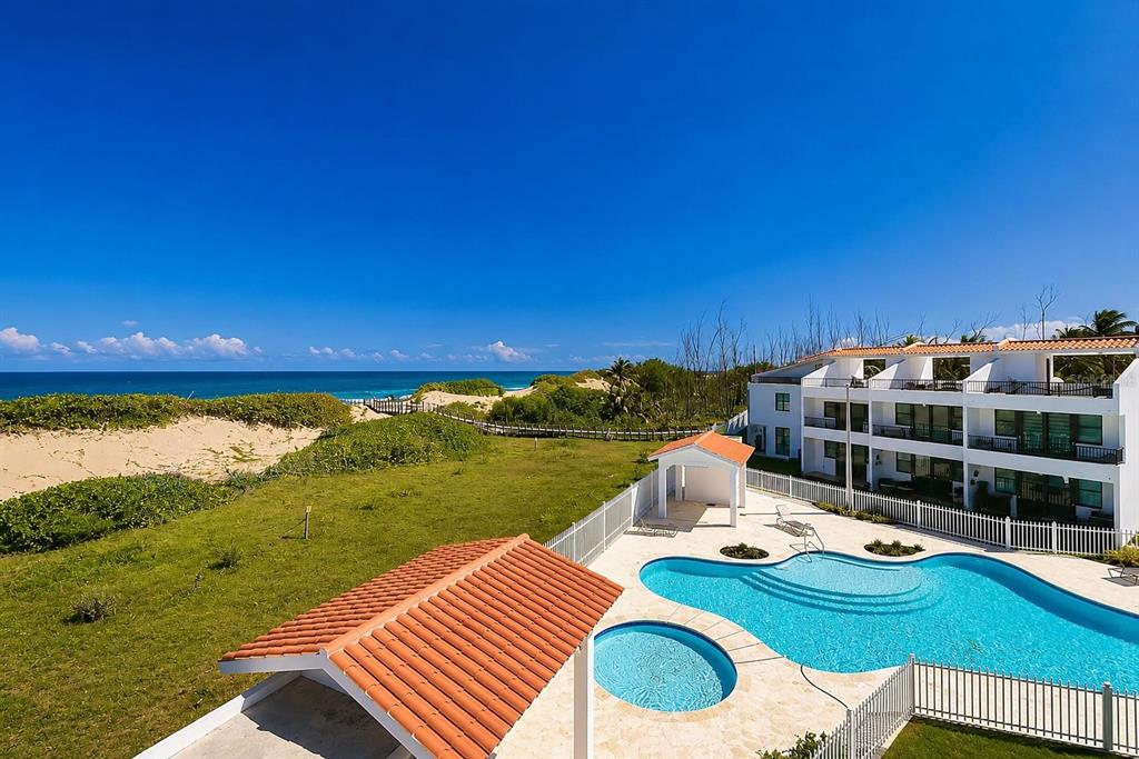 An outdoor swimming pool sits next to a white apartment building near a sandy beach — 348 PR-4466 MARBELA CASA DE PLAYA UNIT C-215, ISABELA, PR