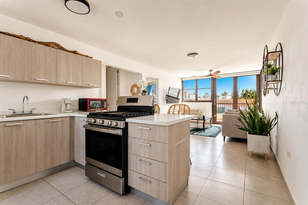A kitchen with light wood cabinets and a stainless steel stove opens to a living area — 348 PR-4466 MARBELA CASA DE PLAYA UNIT C-215, ISABELA, PR