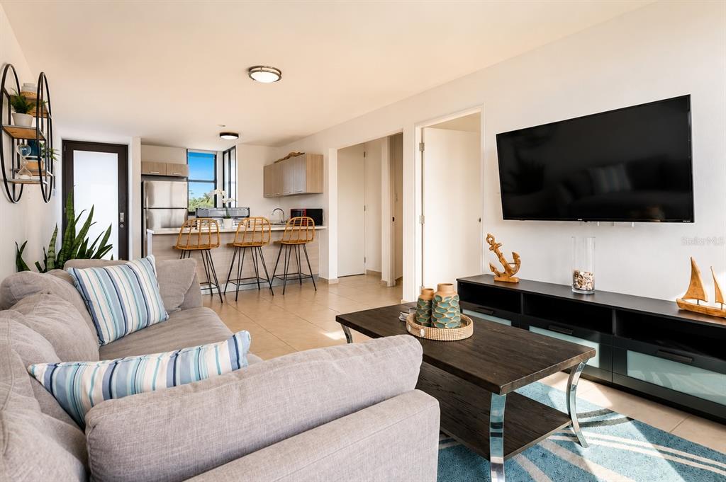 A living room with a grey sofa, coffee table, and television opens to a kitchen area — 348 PR-4466 MARBELA CASA DE PLAYA UNIT C-215, ISABELA, PR