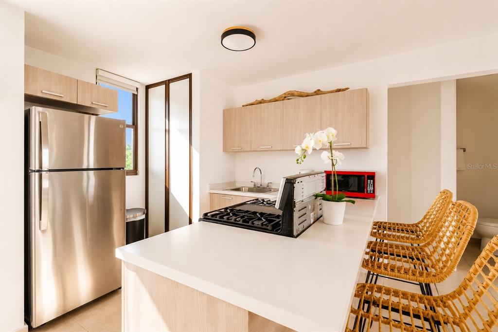 A kitchen features light wood cabinets, a stainless steel refrigerator, and a white island — 348 PR-4466 MARBELA CASA DE PLAYA UNIT C-215, ISABELA, PR