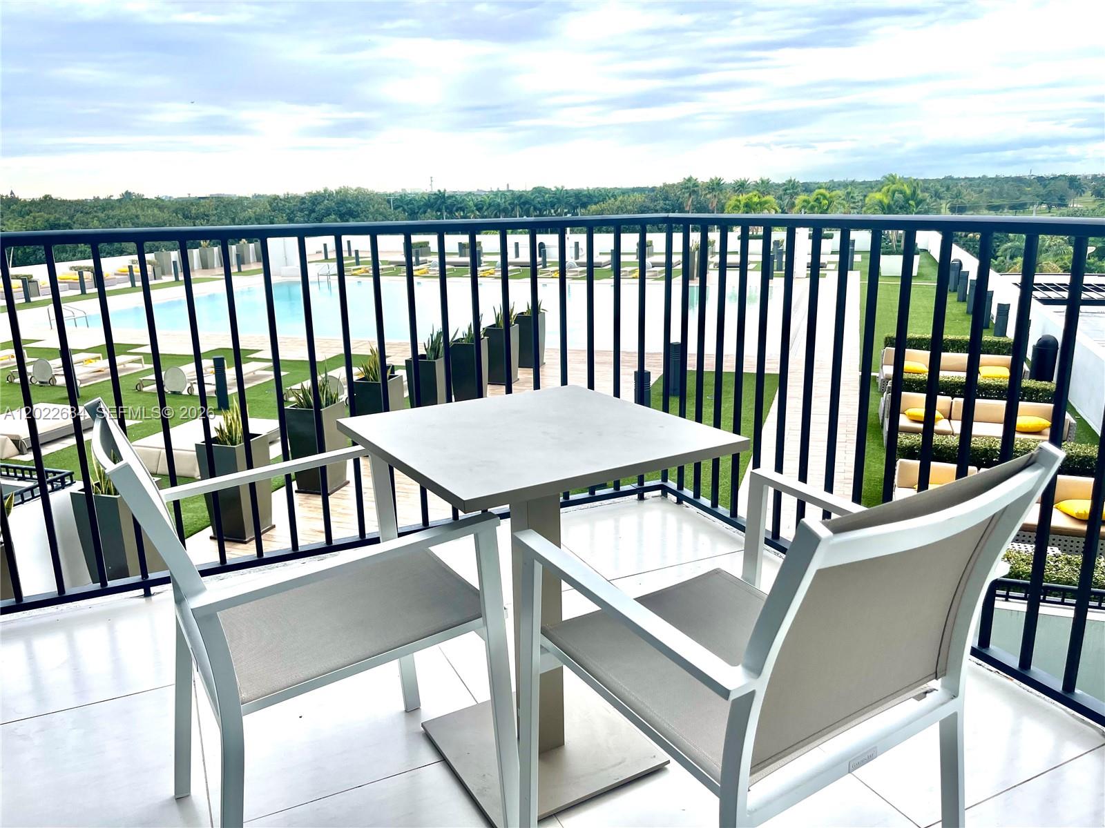 A balcony with a table and two chairs overlooks a swimming pool and green landscape — 5252 NW 85th Ave # 406, Doral FL 33166, DORAL, FL