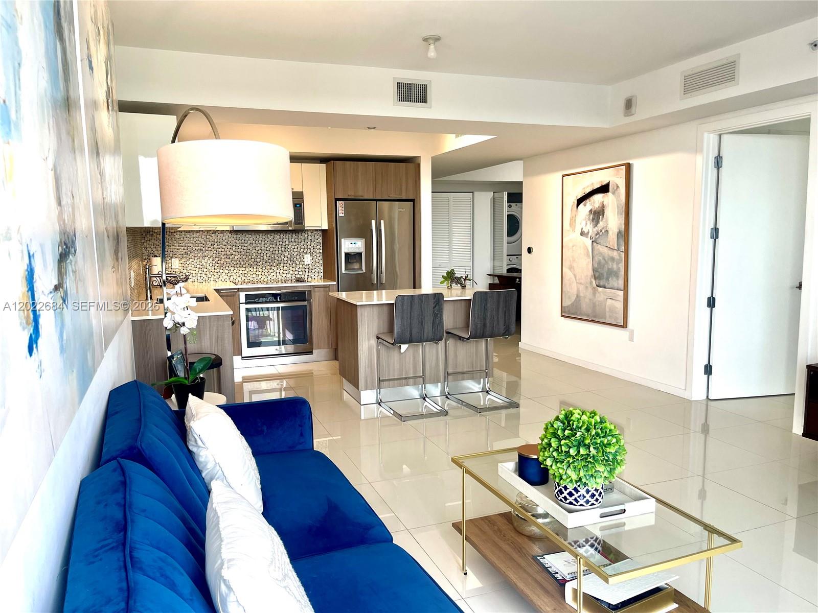 A modern living room and kitchen area feature a blue sofa, island seating, and tile floors — 5252 NW 85th Ave # 406, Doral FL 33166, DORAL, FL