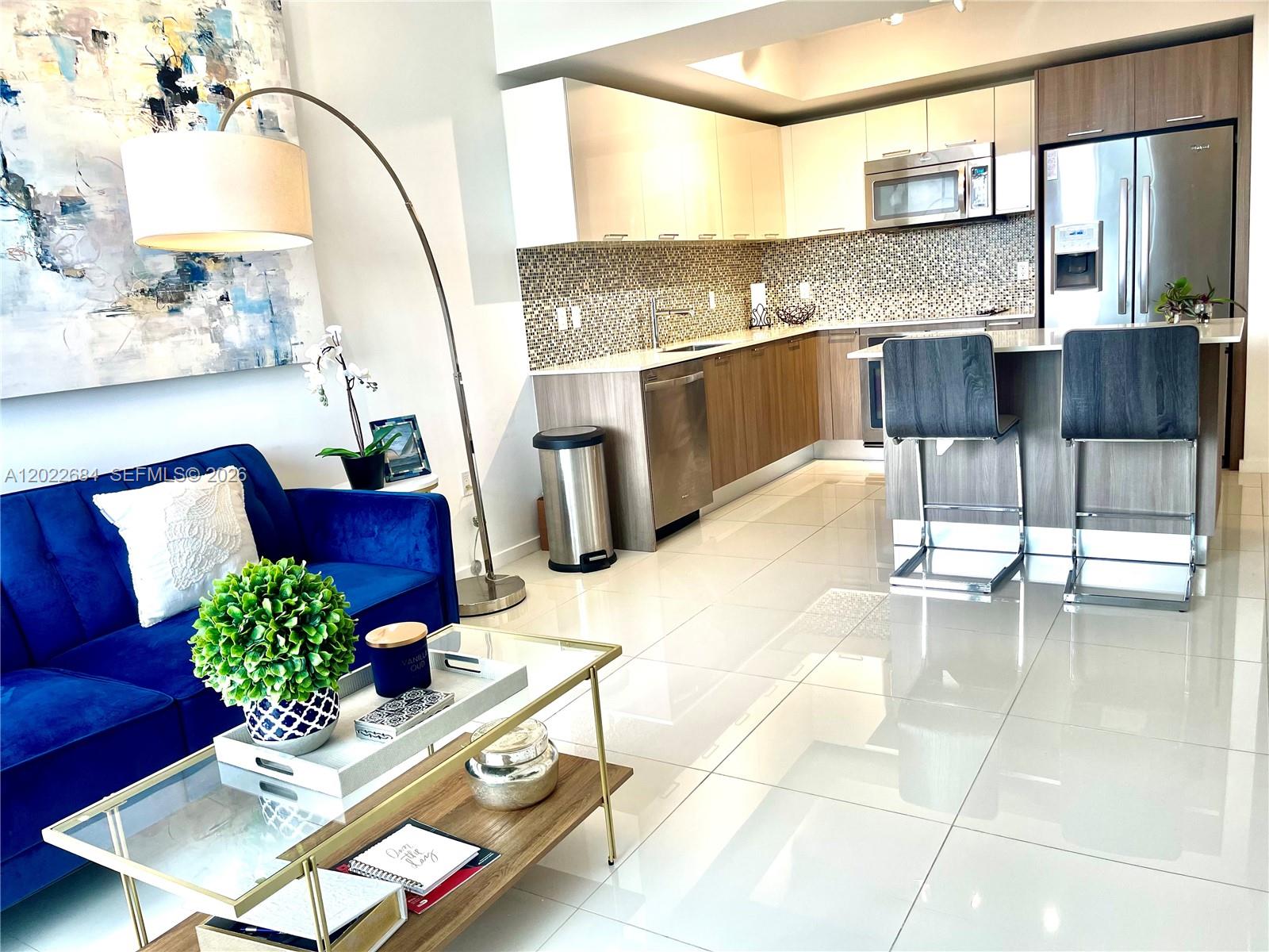 A modern open-concept living room and kitchen with white tile floors and blue sofa — 5252 NW 85th Ave # 406, Doral FL 33166, DORAL, FL