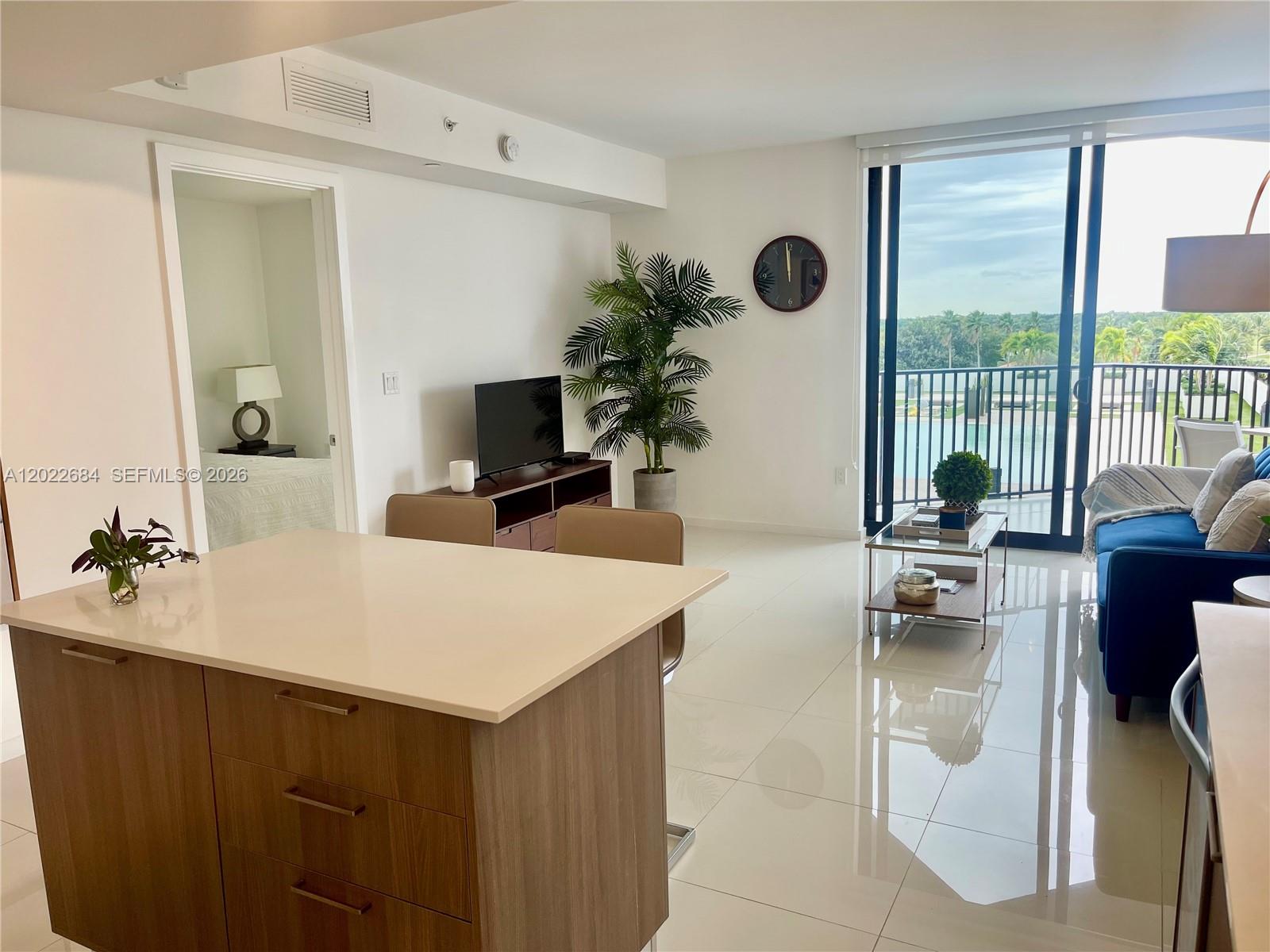 A modern living room features white tile floors, a kitchen island, and a balcony view — 5252 NW 85th Ave # 406, Doral FL 33166, DORAL, FL