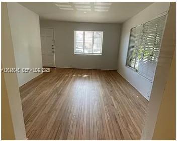An empty living room features light-colored hardwood floors, white walls, and a large window — 23 Majorca Ave # 1, Coral Gables FL 33134, CORAL GABLES, FL
