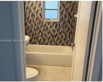 A bathroom features a white bathtub, a toilet, and a wall with patterned tile — 23 Majorca Ave # 1, Coral Gables FL 33134, CORAL GABLES, FL