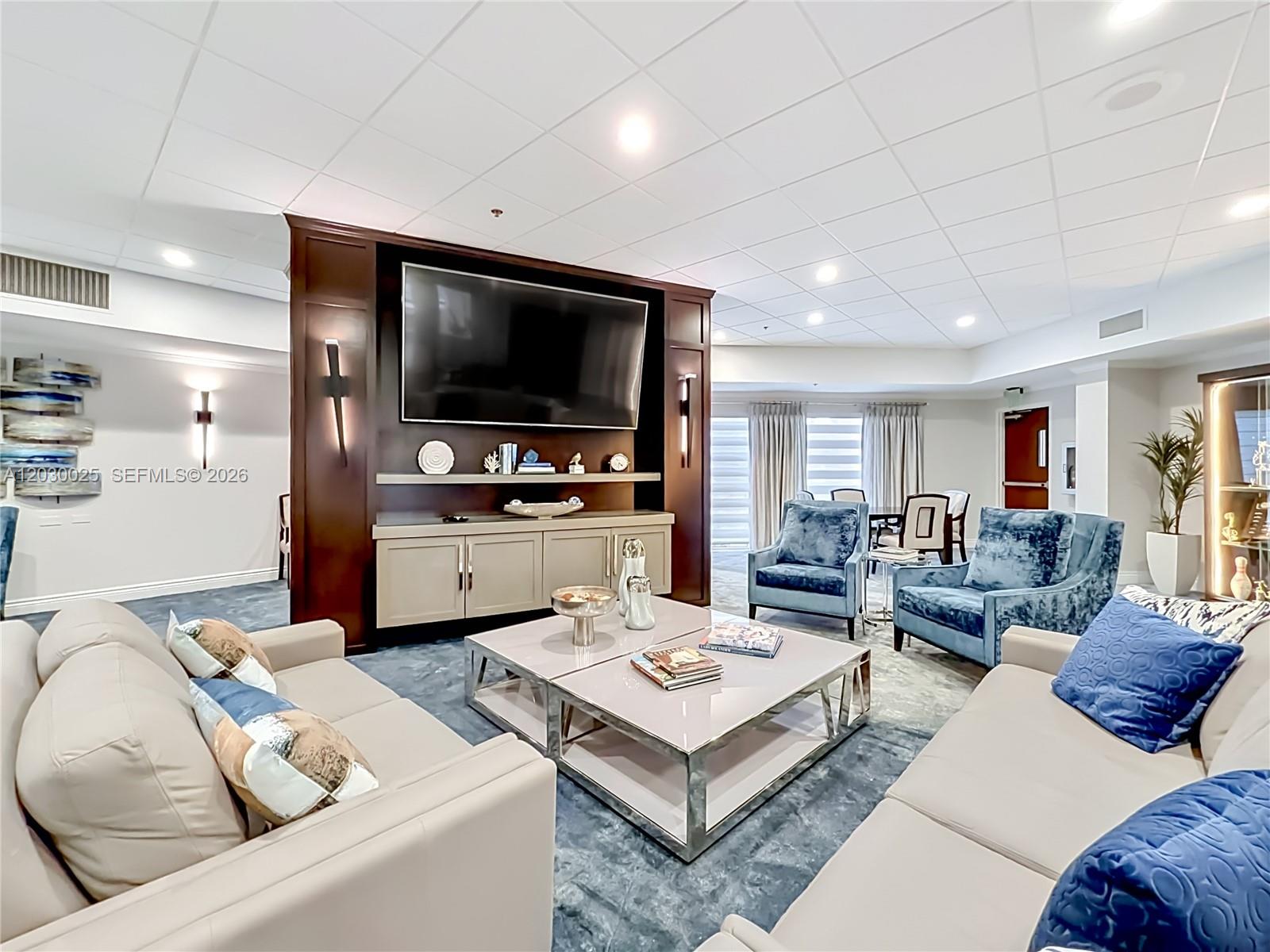 A living room features a large television, two beige sofas, and two blue velvet chairs — 5591 Royal Lake Cir, Boynton Beach FL 33437, BOYNTON BEACH, FL