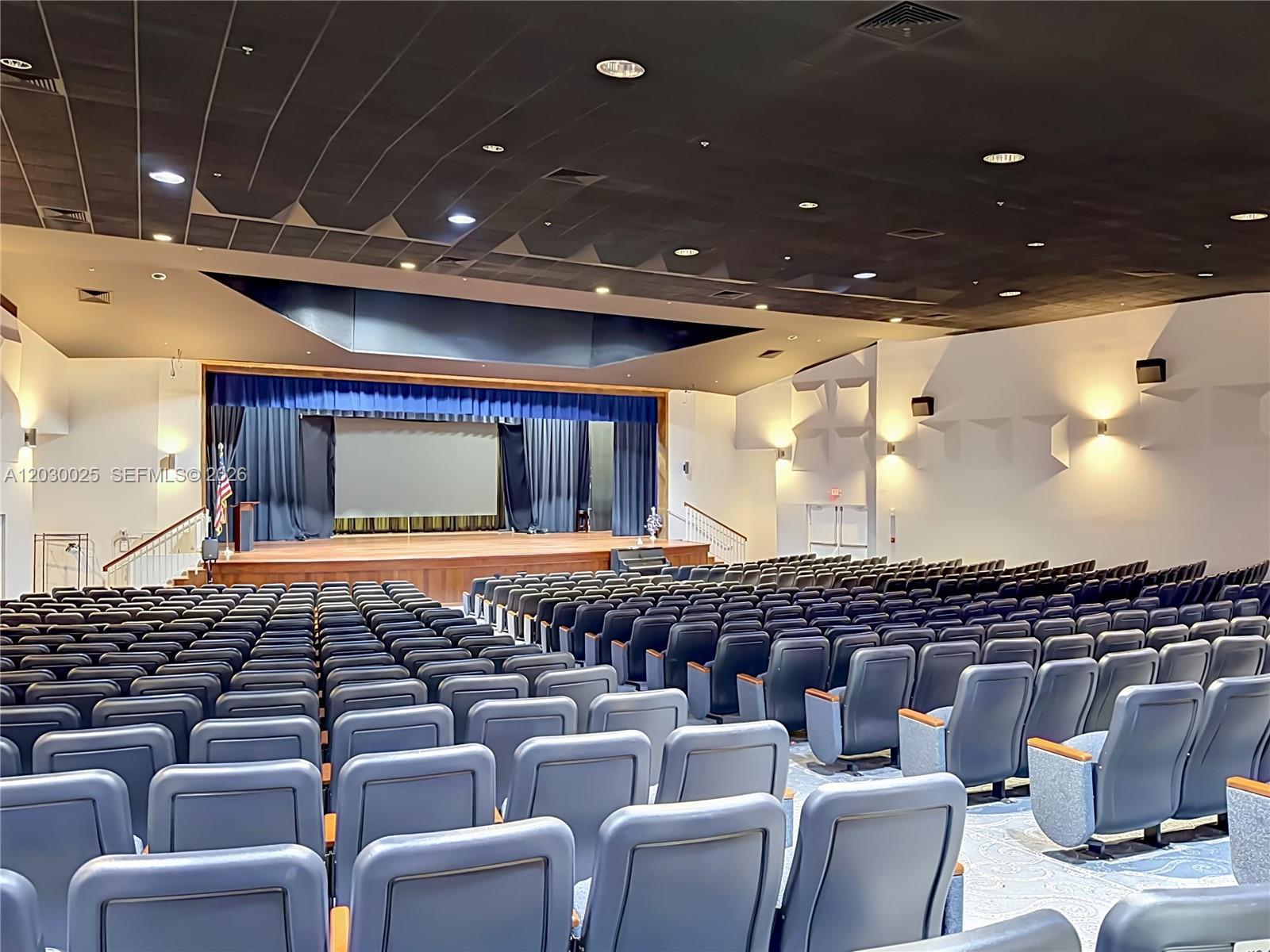An auditorium features rows of blue seats facing a stage with a screen and curtains — 5591 Royal Lake Cir, Boynton Beach FL 33437, BOYNTON BEACH, FL