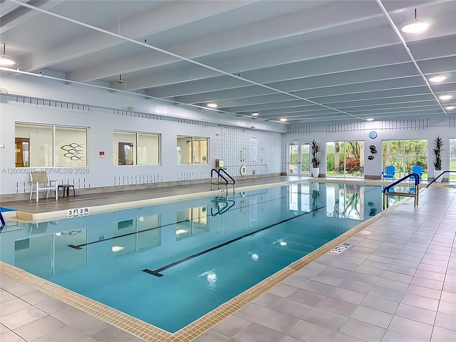 An indoor swimming pool features light blue water, tiled flooring, and large windows along the wall — 5591 Royal Lake Cir, Boynton Beach FL 33437, BOYNTON BEACH, FL