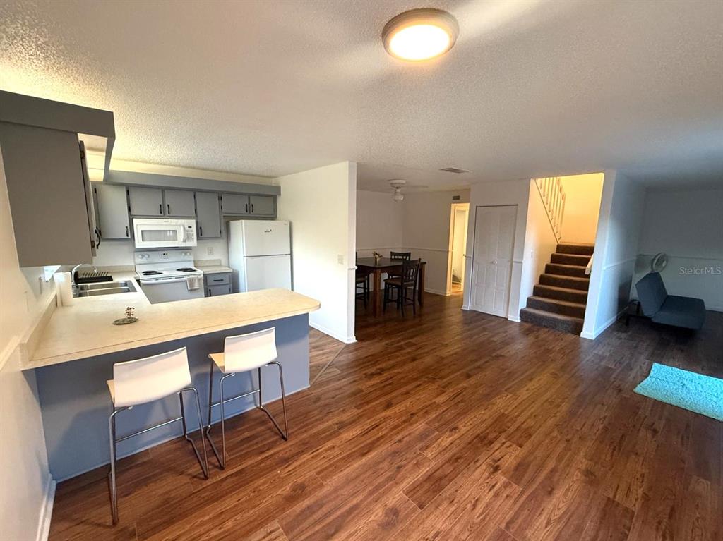 A kitchen with a breakfast bar overlooks a dining area and a carpeted staircase — 1406 PARK SHORE CIRCLE UNIT 3, FORT MYERS, FL