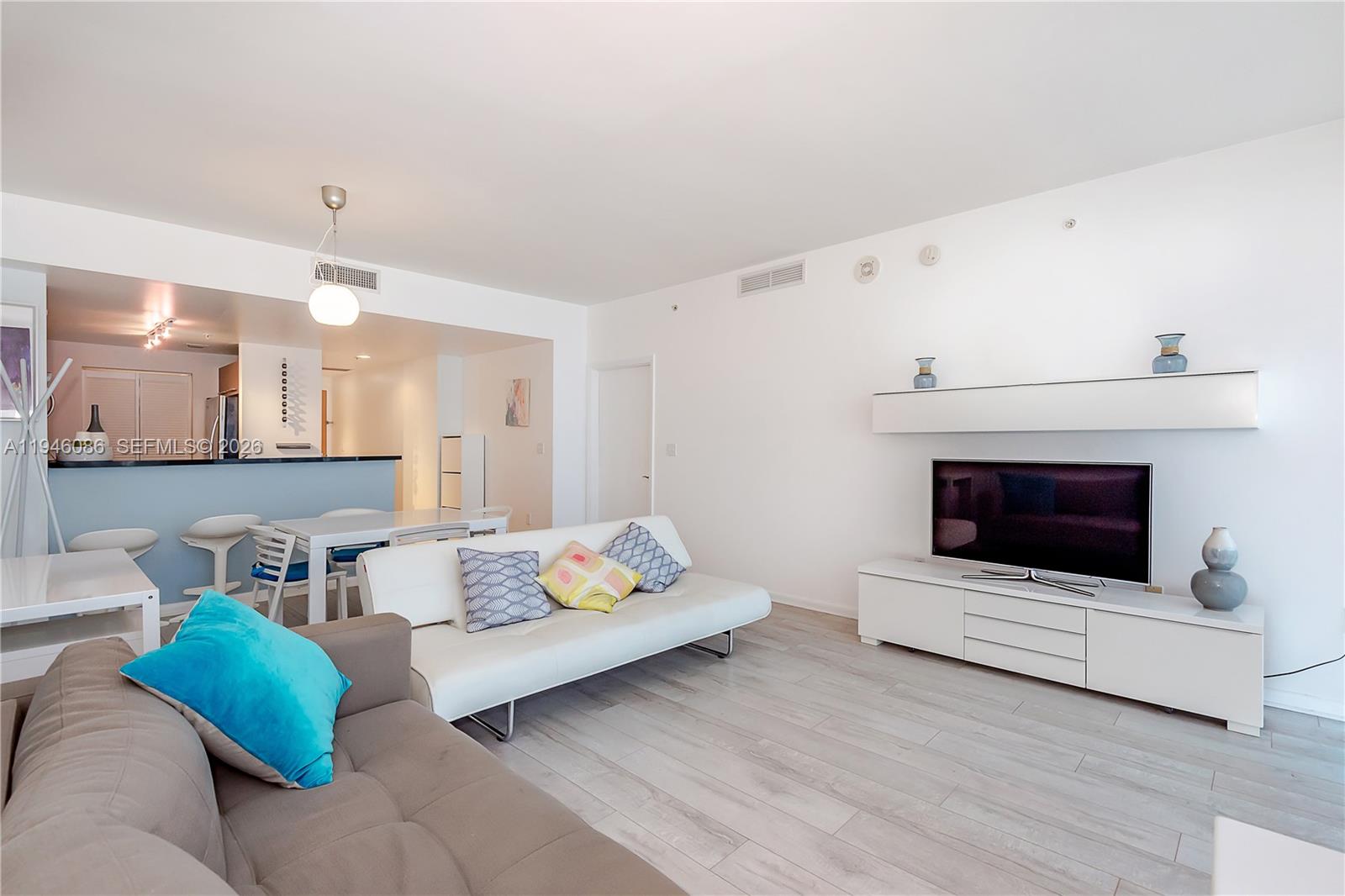 A living room features a white sofa, a television console, and an adjacent dining area — 253 NE 2nd St # 907, Miami FL 33132, MIAMI, FL