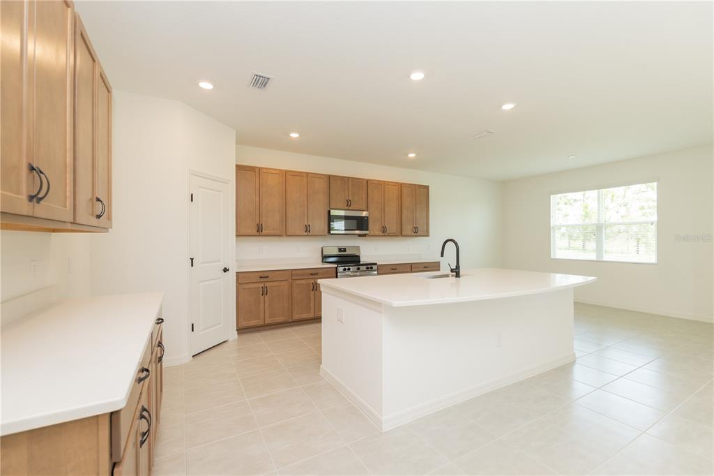 A kitchen features light wood cabinets, white countertops, a central island, and tile flooring — 3108 EVELYN LANE, BARTOW, FL