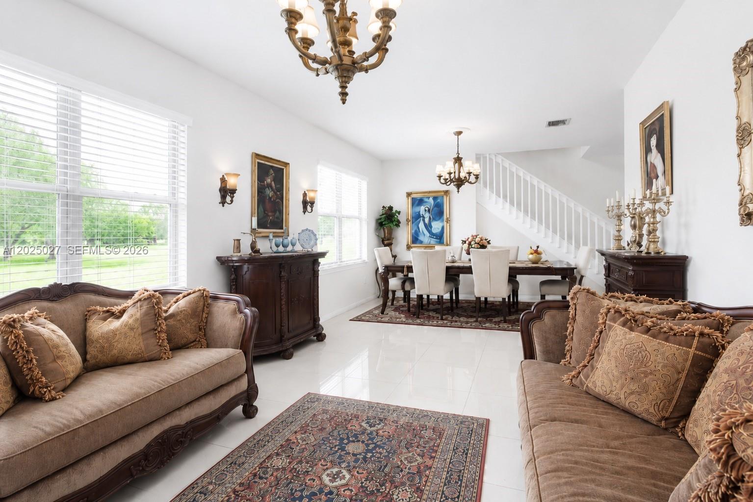 A living and dining area features white tile floors, brown sofas, and two chandeliers — 19220 NE 9th Pl, Miami FL 33179, MIAMI, FL