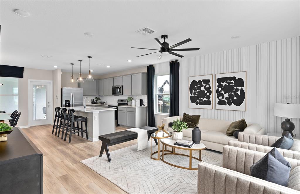 An open-concept living room and kitchen featuring light wood floors, gray cabinetry, and modern decor — 6834 CREEK FALLS ALLEY, CLERMONT, FL