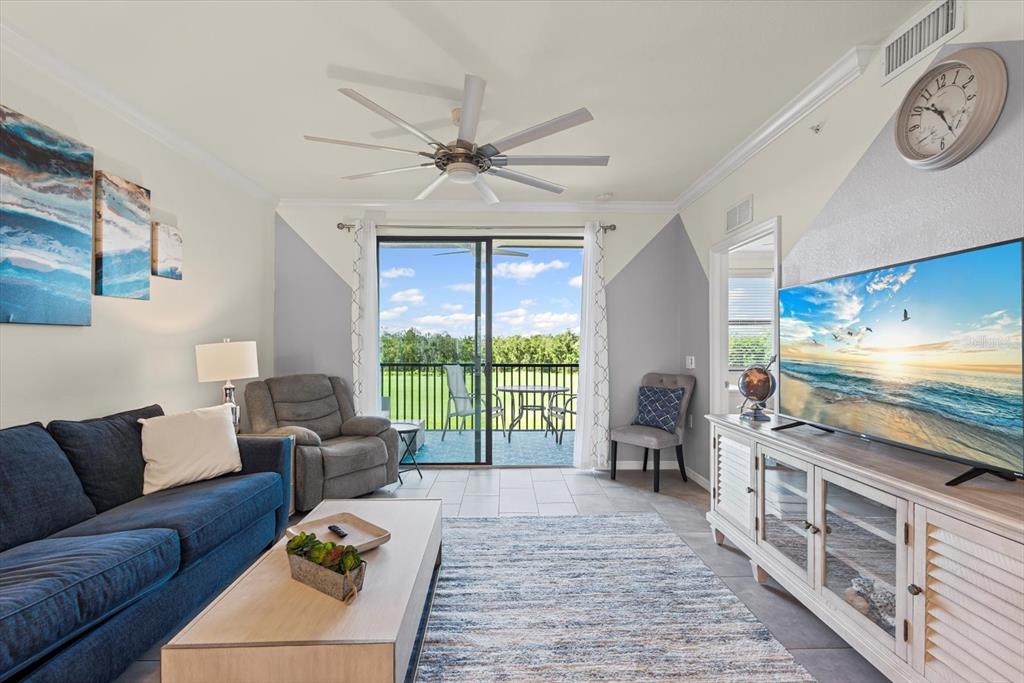 A living room features a blue sofa, a television, a ceiling fan, and a balcony — 17810 GAWTHROP DRIVE UNIT 304, BRADENTON, FL