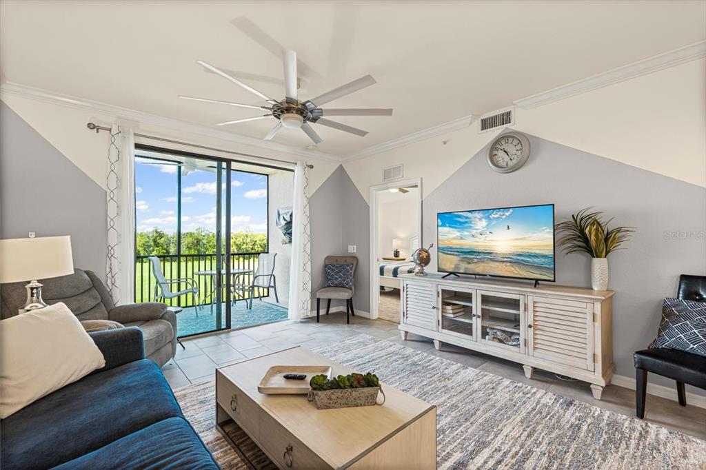 A living room features a ceiling fan, a television on a console, and a balcony — 17810 GAWTHROP DRIVE UNIT 304, BRADENTON, FL