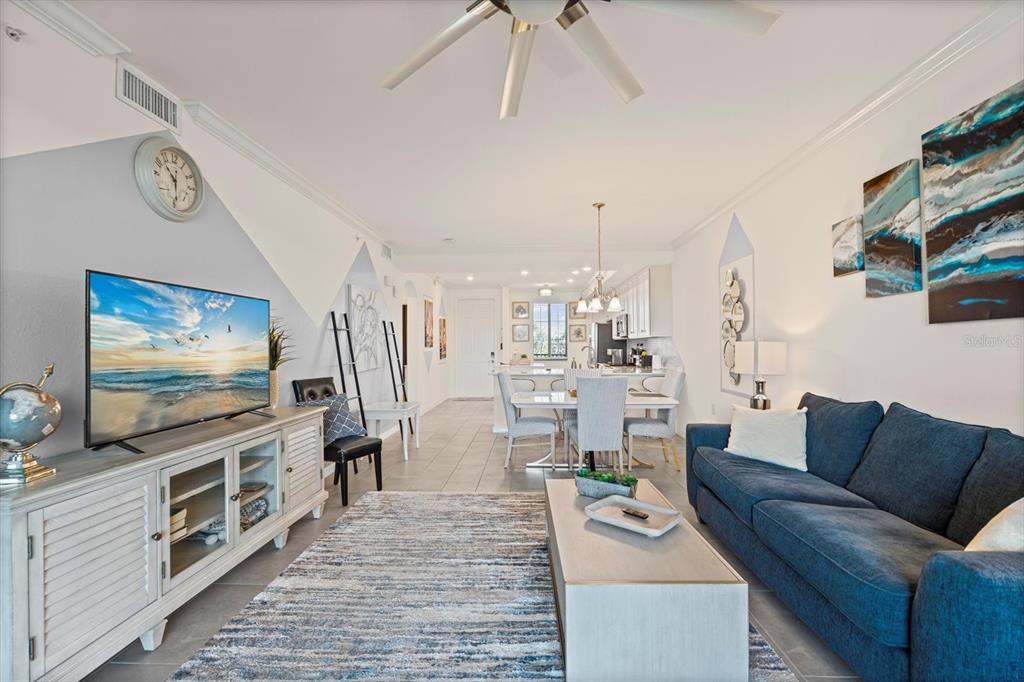 A living room with a blue sofa, television, and dining area on a tiled floor — 17810 GAWTHROP DRIVE UNIT 304, BRADENTON, FL