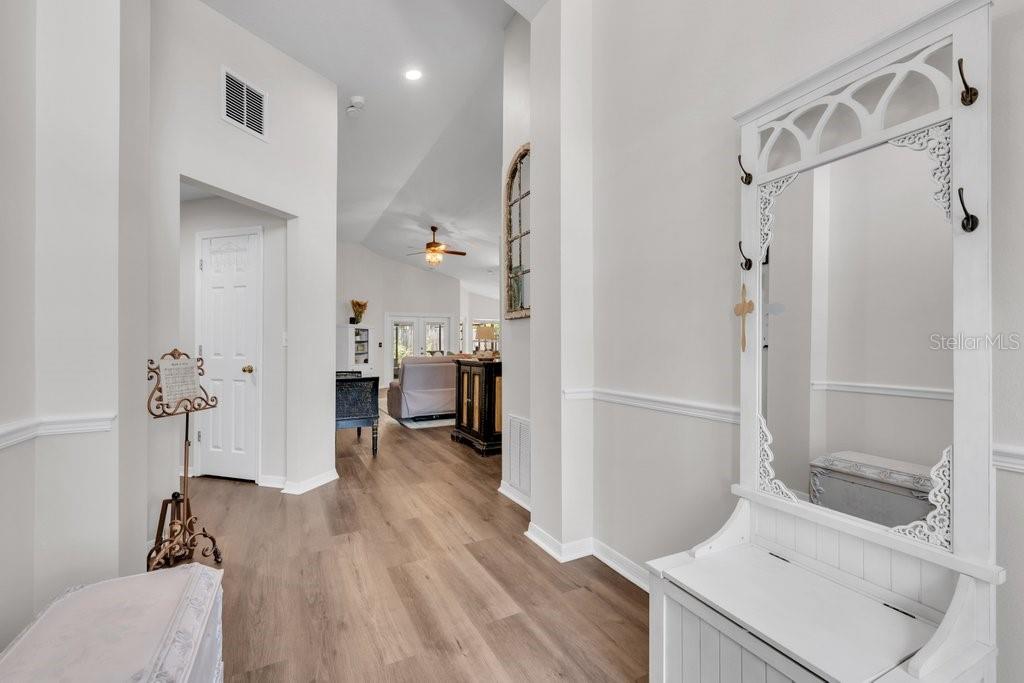 A bright entryway features light wood-look flooring, white walls, and a white hall tree mirror — 1924 SEDGEFIELD STREET, BRANDON, FL