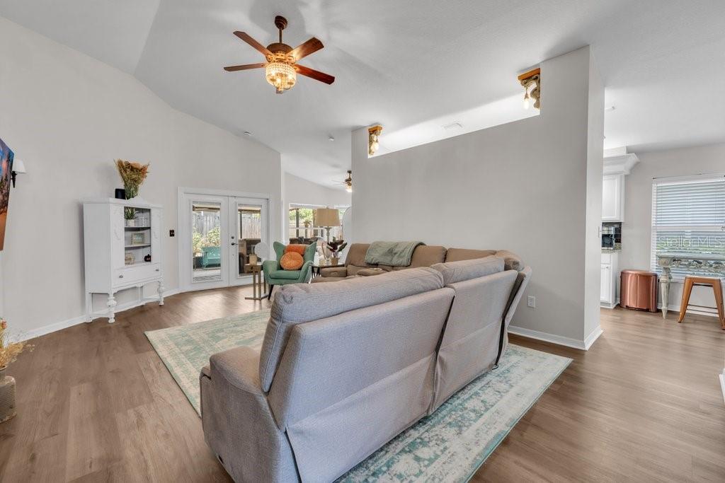 A living room with light wood floors, a gray sofa, and a vaulted ceiling — 1924 SEDGEFIELD STREET, BRANDON, FL