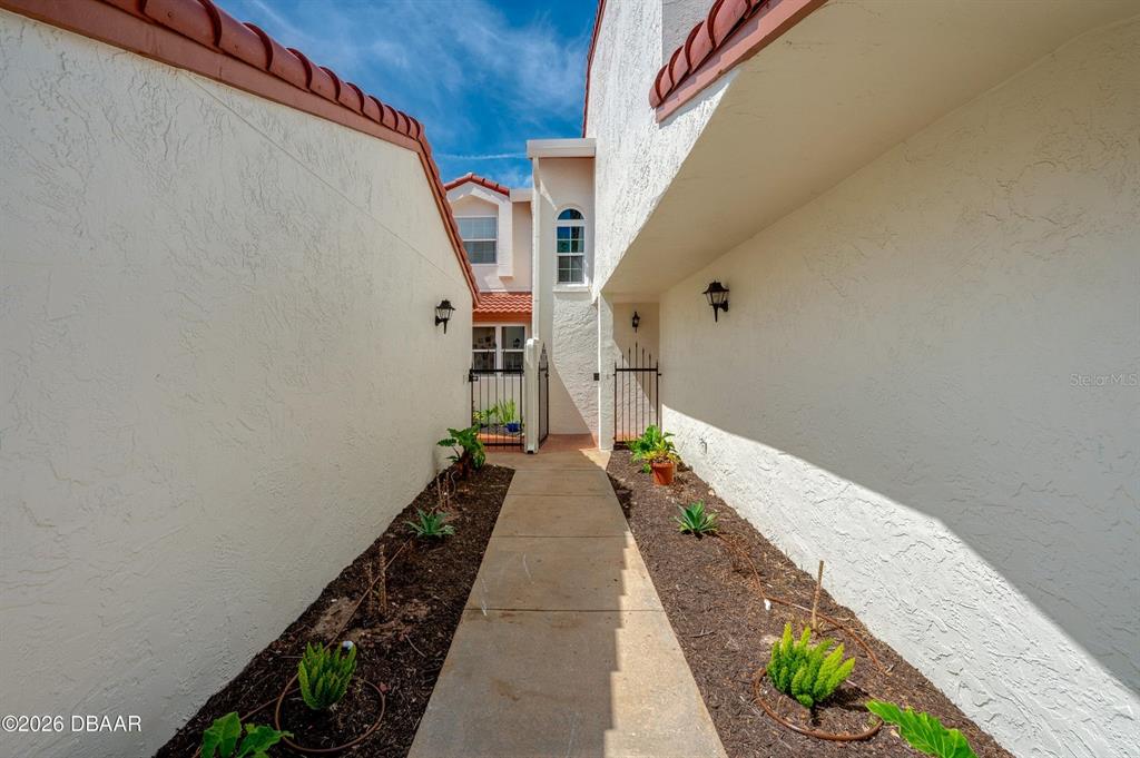 A narrow concrete walkway leads between two stucco walls toward a gated courtyard entrance — 226 FLORIDA SHORES BOULEVARD, DAYTONA BEACH, FL