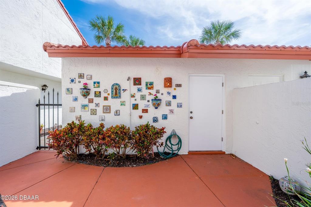 An exterior view shows a white wall decorated with tiles, a door, and landscaping — 226 FLORIDA SHORES BOULEVARD, DAYTONA BEACH, FL