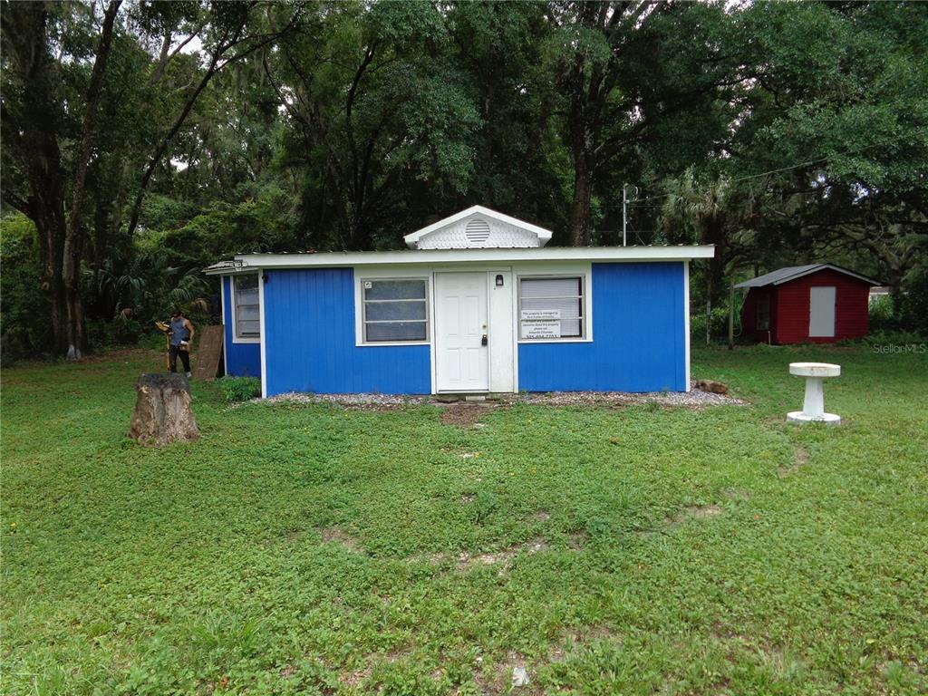 A small, blue, single-story house with a white door stands in a grassy, wooded yard — 2878 NE 161ST STREET, CITRA, FL