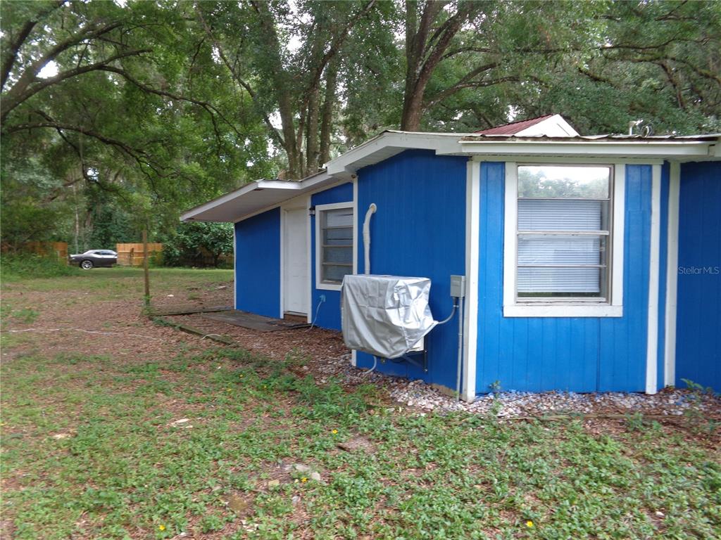 The exterior of a blue house features a window, a door, and a covered air conditioner — 2878 NE 161ST STREET, CITRA, FL