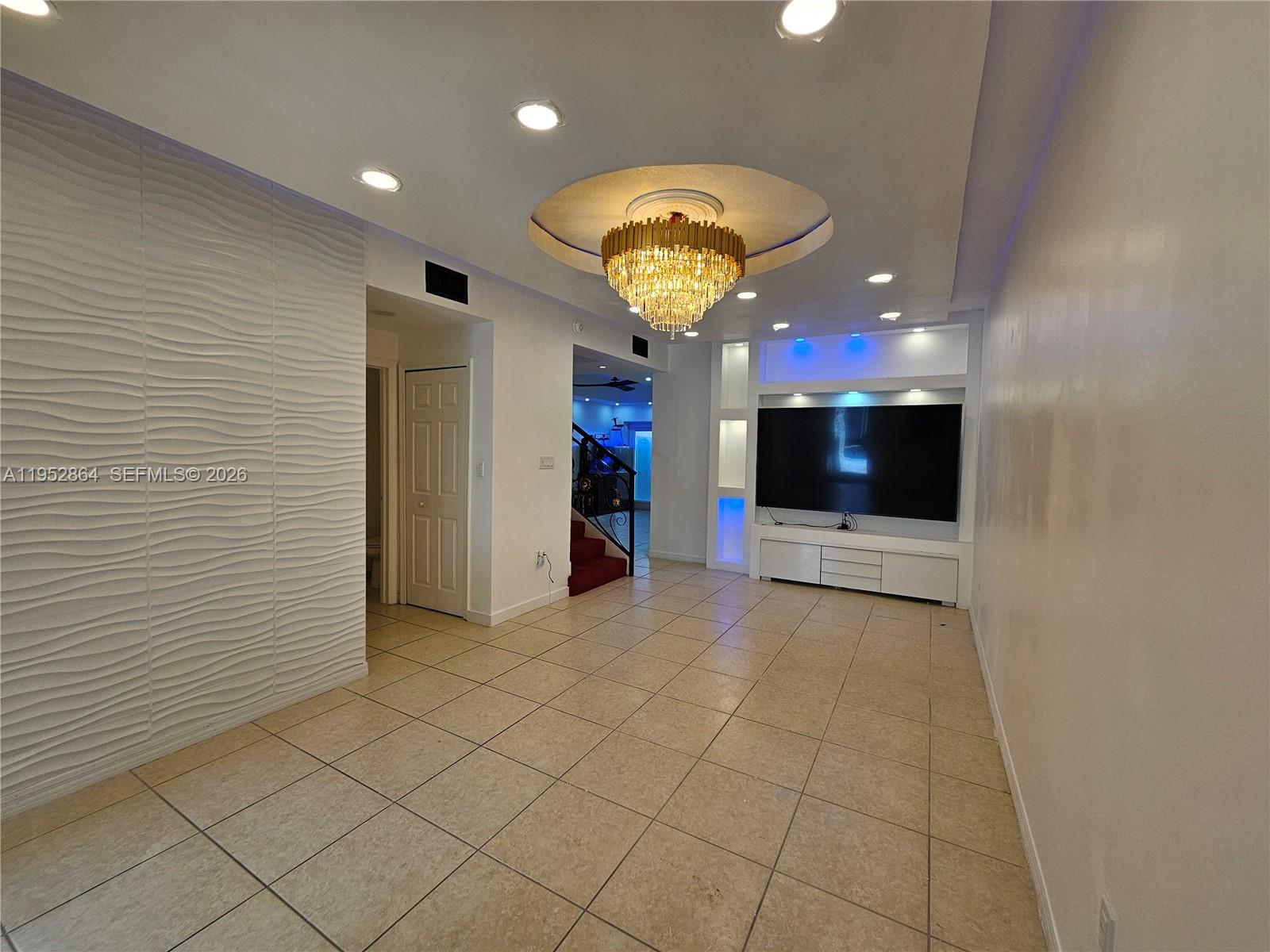A living room features a textured accent wall, a crystal chandelier, and a media console — 8371 SW 124th Ave # 12, Miami FL 33183, MIAMI, FL