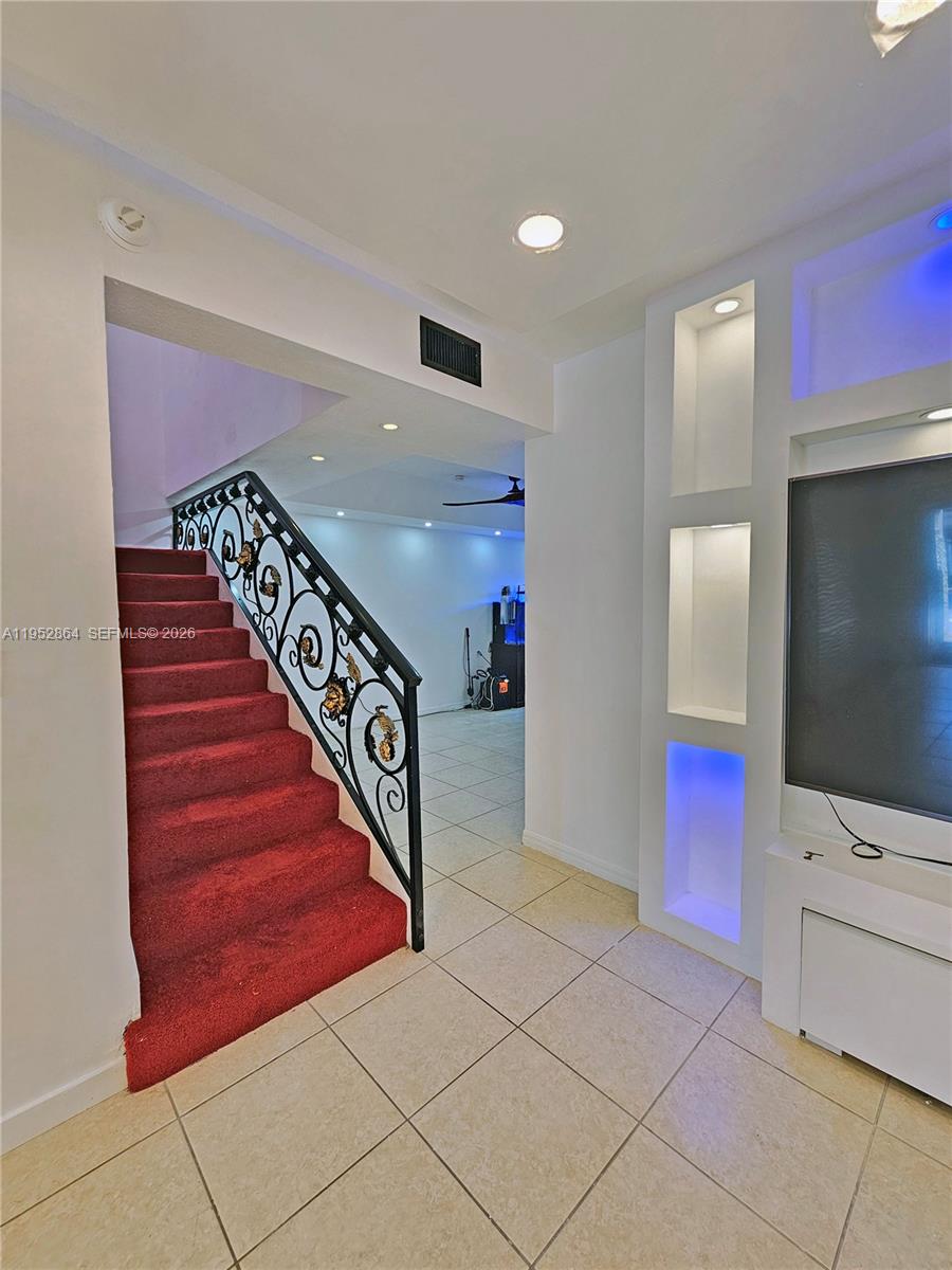 A staircase with red carpeting and a decorative metal railing sits beside a media wall — 8371 SW 124th Ave # 12, Miami FL 33183, MIAMI, FL