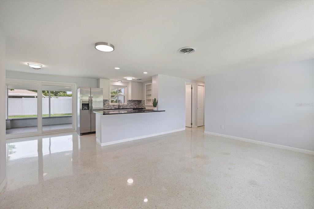 A bright, open-concept kitchen and living area featuring white walls, polished terrazzo floors, and stainless-steel appliances — 3485 ROSLYN ROAD, VENICE, FL