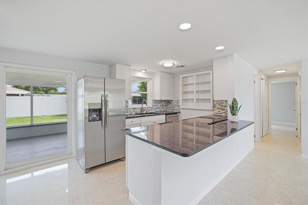 A kitchen with white cabinets, stainless steel appliances, a dark granite island, and terrazzo flooring — 3485 ROSLYN ROAD, VENICE, FL