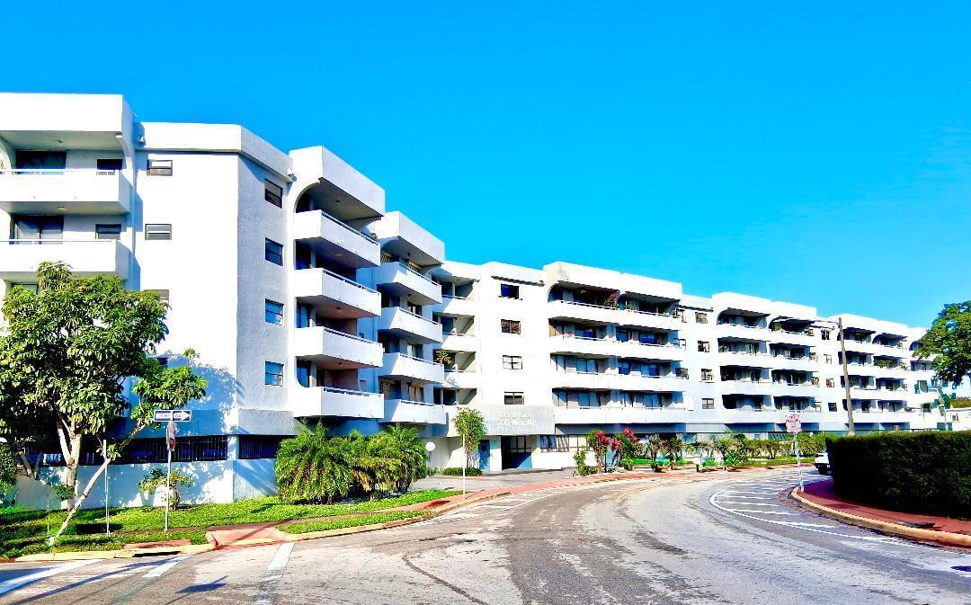 A multi-story white apartment building with balconies stands along a curved road under a sky — 7300 Wayne Avenue # 213, Miami Beach FL 33141, MIAMI BEACH, FL