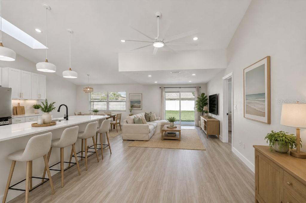 An open-concept living room and kitchen feature white cabinetry, light wood flooring, and sliding doors — 6501 68TH DRIVE E, PALMETTO, FL