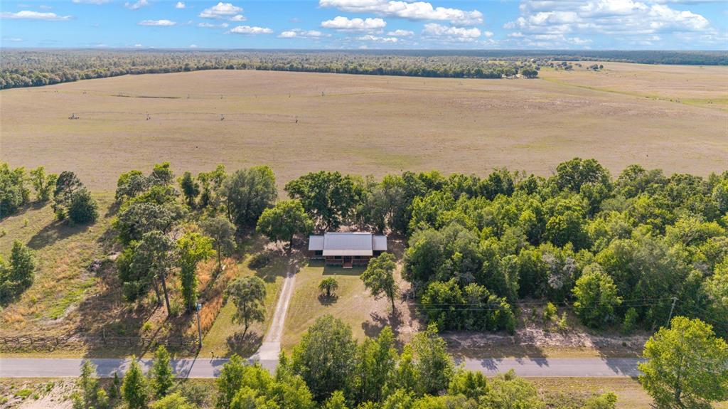An aerial view shows a house nestled among trees next to a large open field — 1230 SW VALENCIA HEIGHTS AVENUE, DUNNELLON, FL